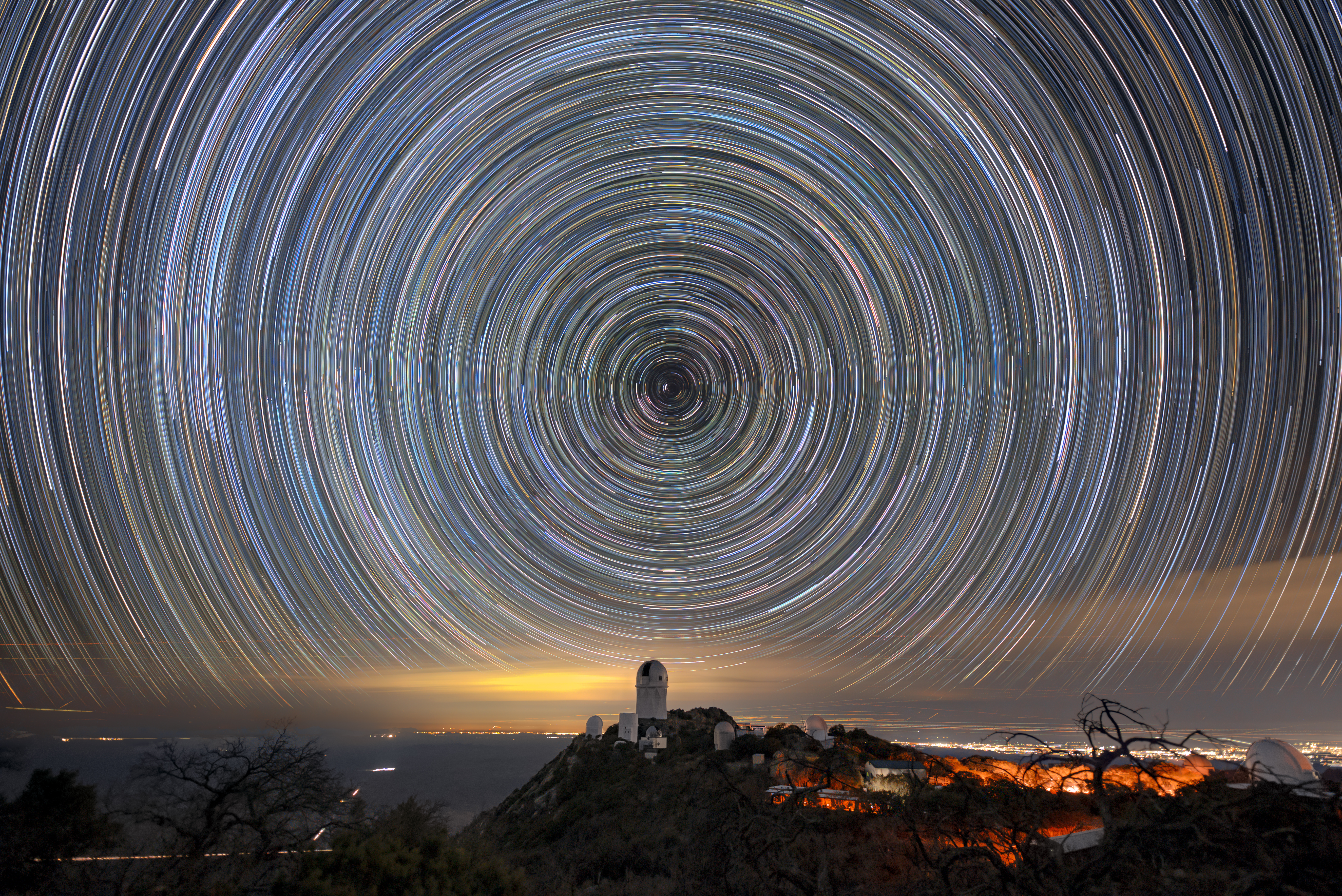 Círculos de luz en el cielo nocturno. La cúpula de un telescopio encima de una montaña está debajo del centro del círculo