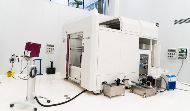 A large white machine with two big doors (polishing machine for large surfaces) in a white room with high ceilings (IACTEC's south clean room).